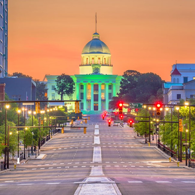 View of Alabama State Capitol building in Montgomery, AL, at sunset with empty street and glowing city lights