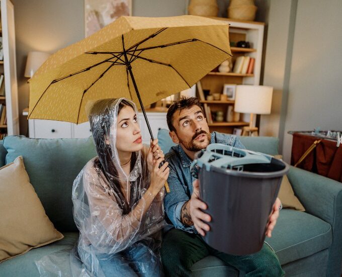 Couple sitting on couch with umbrella and bucket catching water from roof leak in Montgomery, AL